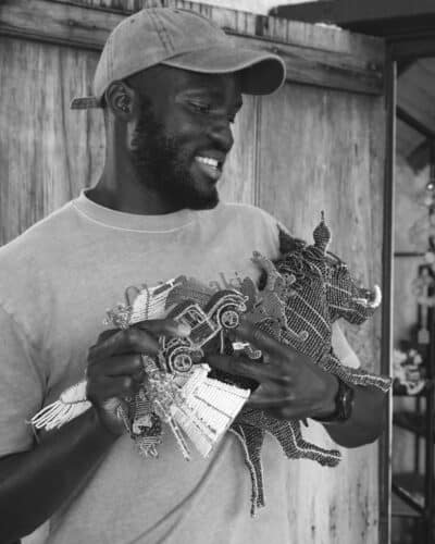 Black and White Image of Tinashe holding his bead and wire sculptures at Old Nick Village