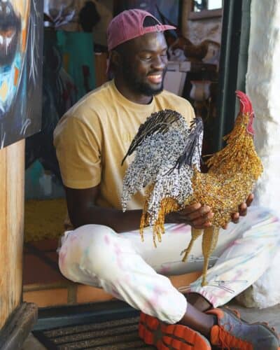 Tinashe, Paivepo's owner, holding a bead and wire chicken sculpture in a door way